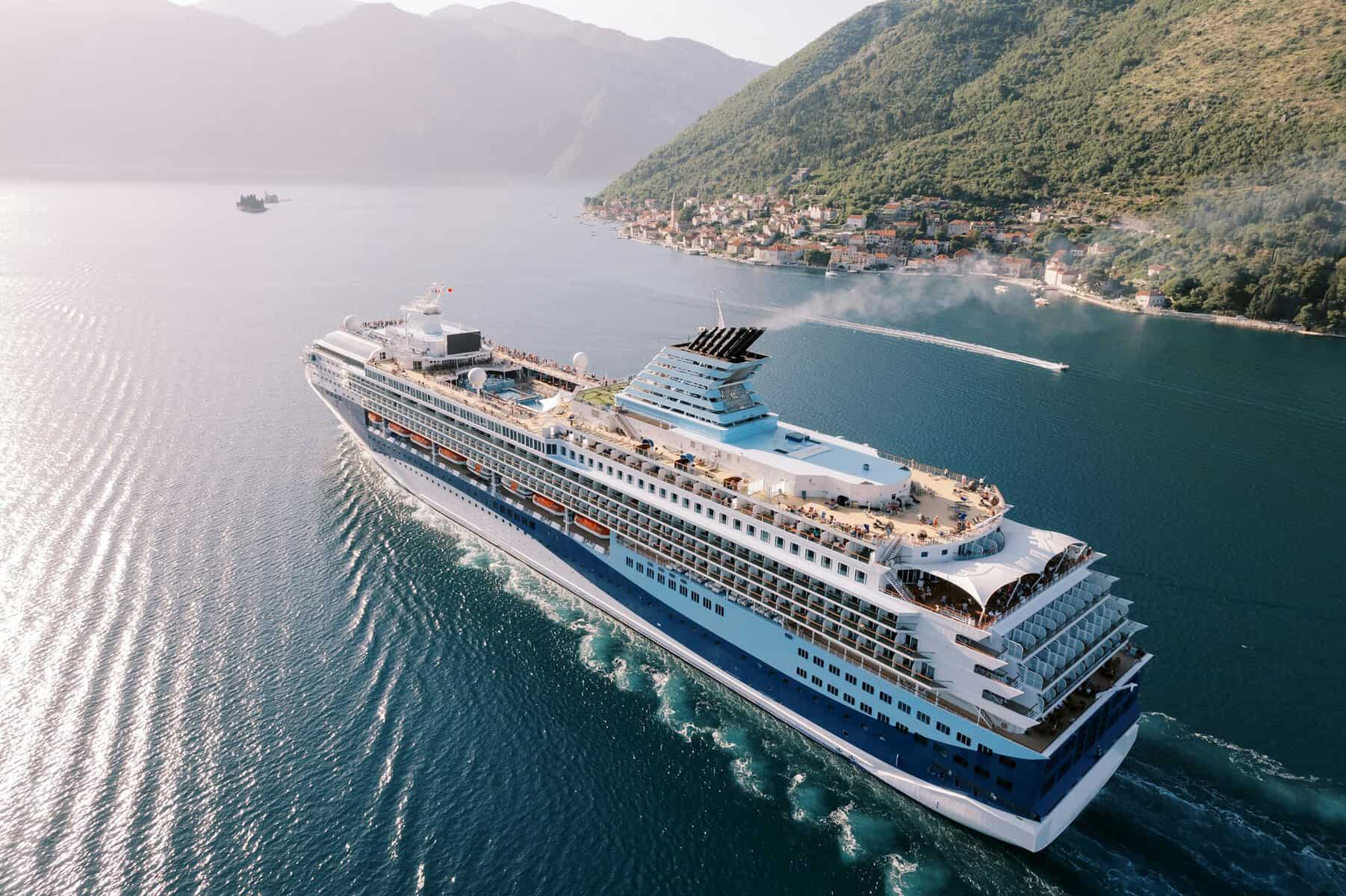 Tall, huge cruise ship sails across the blue sea along a mountainous coastline. Drone