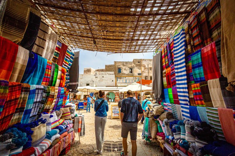 Tourists walking through Moroccan market of colourful throws