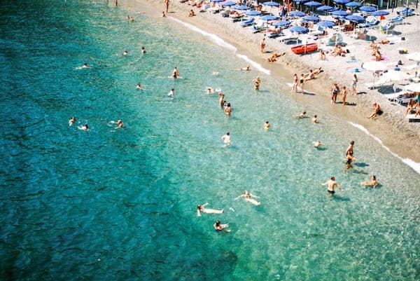 7-Day Amalfi Coast Itinerary: Planned Around How It Feels To Be There 8 Aerial View Of A Beach With Turquoise Waters On The Amalfi Coast. People Swim And Relax Under Blue Umbrellas On The Sandy Shore, Capturing A Lively, Sunny Atmosphere.